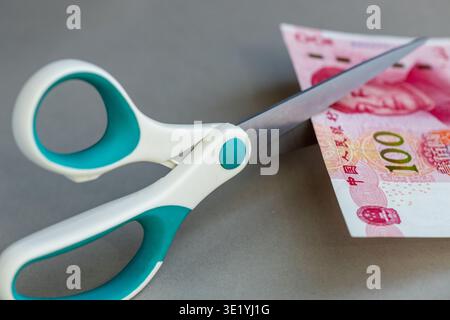 Argent chinois. Ciseaux coupant le Yuan chinois. Valeur décroissante. Concept financier et commercial. Analyse des coûts. Gros plan Banque D'Images