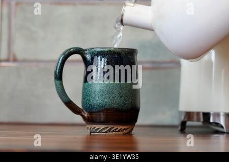 L'eau bouillante étant versée dans une tasse verte faite à la main dans une cuisine moderne rustique Banque D'Images