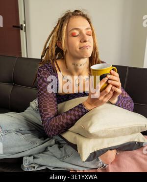 Jeune femme se relaxant sur le canapé, tenant une tasse de café chaud ou de thé avec les yeux fermés Banque D'Images