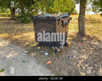Evesham, Worcestershire, Angleterre, Royaume-Uni - 24 août 2025 : grande poubelle industrielle dans un parc rural avec des déchets dispersés autour de lui. Banque D'Images