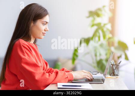 Femme travaille sur ordinateur portable à un bureau près des plantes pendant les heures de jour dans une pièce lumineuse Banque D'Images