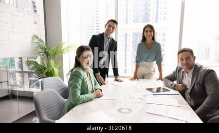 Équipe de professionnels multiethniques motivés posant autour de la table dans le bureau en verre Banque D'Images