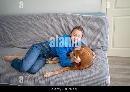Aimant femme mature propriétaire d'animal de compagnie se relaxant sur le canapé avec le chien bien-aimé, caressant doucement le chien endormi d'humeur sombre. Banque D'Images