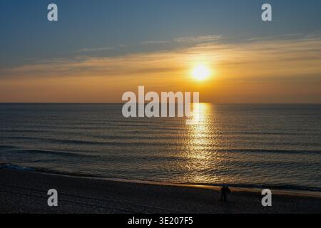 Coucher de soleil chaud sur la mer Baltique avec des reflets dorés sur l'eau et un couple marchant le long de la plage de sable au crépuscule Banque D'Images