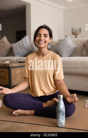 Femme souriante méditant à la maison sur tapis de yoga Banque D'Images