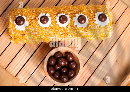 Délicieux gâteau roulé recouvert de noix et de crème avec des boules de chocolat et Un bol de bonbons au chocolat sur Une table en bois Banque D'Images