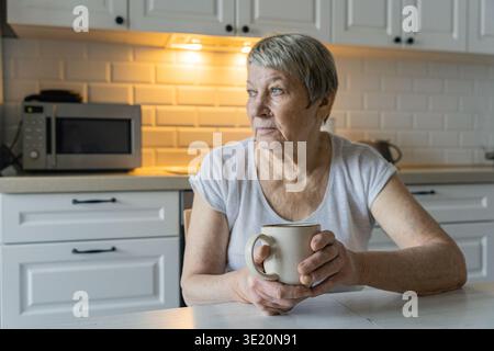 Femme âgée buvant du café contemplant dans la cuisine Banque D'Images