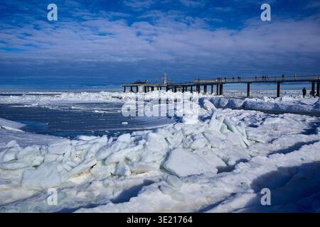 Une vue panoramique époustouflante sur la mer Baltique gelée, mettant en valeur une jetée moderne s'étendant dans une vaste étendue de glace de mer et une plage enneigée. LAR Banque D'Images