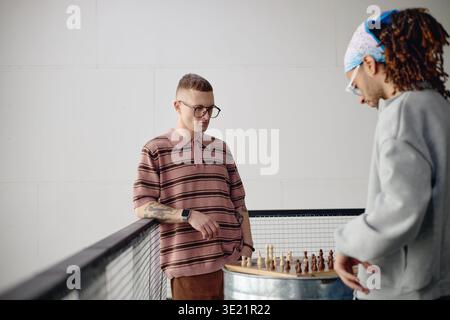 Jeune homme adulte jouant aux échecs avec un ami masculin biracial à l'intérieur Banque D'Images
