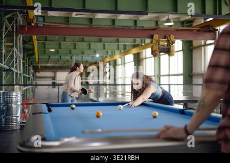 Jeune femme jouant au billard avec des amis dans un cadre industriel Banque D'Images