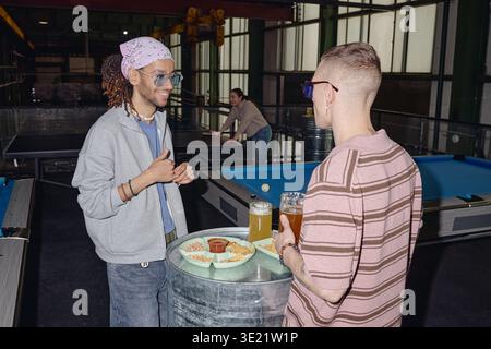Jeunes hommes adultes socialisant et buvant de la bière près de la table de billard à l'intérieur Banque D'Images