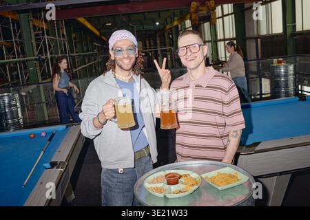 Divers amis masculins jeunes adultes appréciant la bière et les collations au club de billard Banque D'Images
