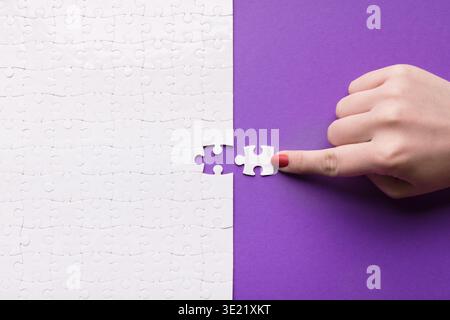 Pièces de puzzle se réunissant sur un fond violet lumineux avec une main plaçant une pièce Banque D'Images