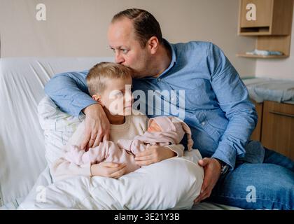 Père embrassant son fils aîné tout en tenant la petite fille nouveau-né. Moment familial émotionnel montrant l'amour et le lien entre les frères et sœurs. Banque D'Images
