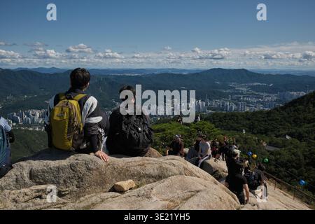 Séoul, Corée du Sud : deux jeunes hommes avec des sacs à dos assis sur des rochers au sommet de Gwanak Mountain bénéficiant d'une vue panoramique sur la ville de Séoul Banque D'Images