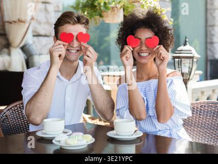 Heureux couple interracial avec des coeurs en papier dans le café Banque D'Images