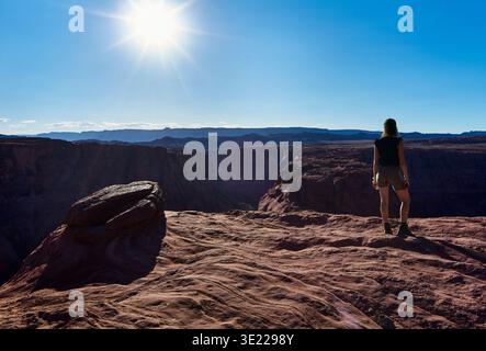 Une personne se tient sur le bord d'une falaise rocheuse, surplombant un canyon sous un ciel ensoleillé. Horseshoe Bend, fleuve Colorado, Arizona, États-Unis Banque D'Images