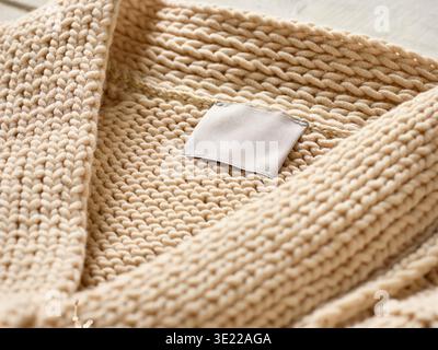 Gros plan d'un pull tricoté beige avec une étiquette blanche vierge sur une surface en bois. Allemagne Banque D'Images