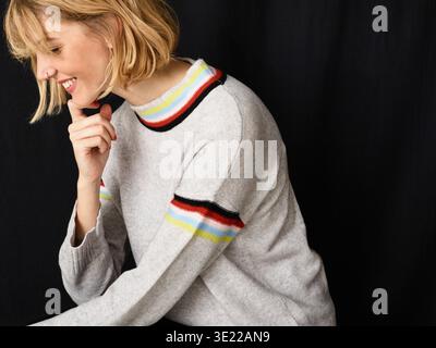 Femme souriant dans un pull rayé sur un fond noir Allemagne Banque D'Images