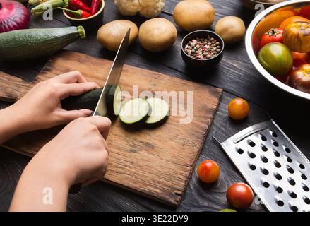 Femme coupant des courgettes vertes sur une planche de bois Banque D'Images
