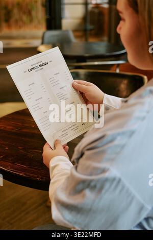 Jeune femme lisant le menu du déjeuner tout en étant assise à l'intérieur du restaurant Banque D'Images