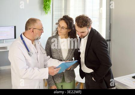 Médecin examinant les résultats médicaux avec couple en clinique, discutant des options du patient Banque D'Images
