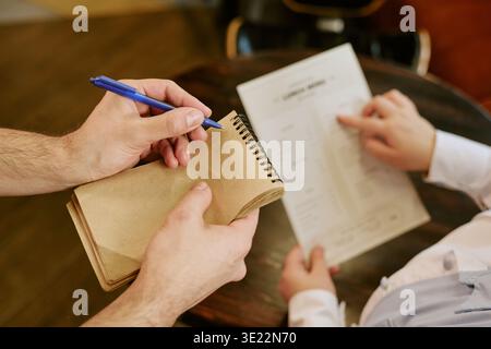 Jeune homme adulte prenant la commande du client tenant le menu du restaurant Banque D'Images
