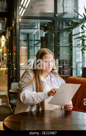 Jeune femme adulte lisant le document tout en étant assis dans le café moderne Banque D'Images