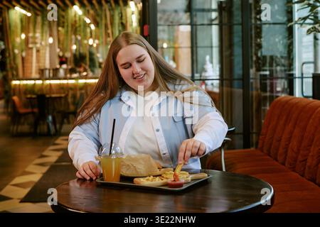Jeune femme adulte souriant en mangeant des frites à l'intérieur Banque D'Images