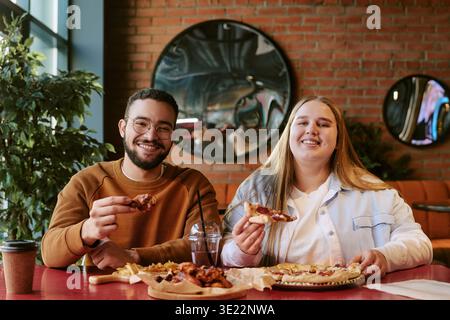 Jeune femme et jeune homme mangeant de la pizza et souriant à la table du restaurant Banque D'Images