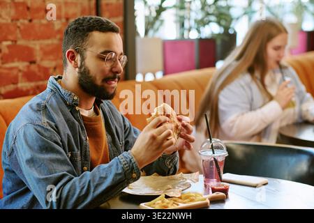 Jeune homme adulte appréciant de manger un hamburger et des frites au restaurant Banque D'Images