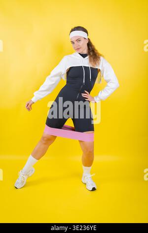 Femme exerçant les jambes avec la bande de résistance sur fond jaune Banque D'Images