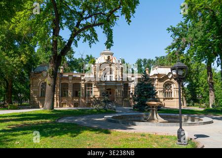 Tachkent (Toshkent), Ouzbékistan (O'zbekiston) - 26 mai 2025 : le Palais historique du Prince Romanov entouré d'arbres verdoyants et d'une fontaine en pierre i. Banque D'Images