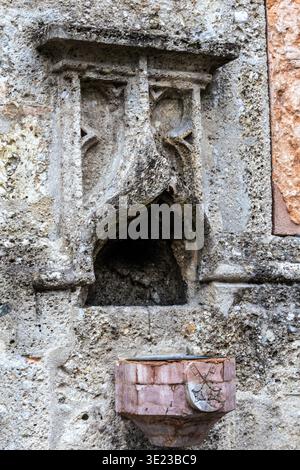 Gros plan d'une fontaine en pierre altérée attachée à un ancien mur de pierre. La fontaine dispose d'un bassin sculpté et d'un bec décoratif en pierre, sh Banque D'Images