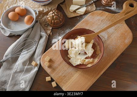 Mélanger le beurre et le sucre dans un bol pour la cuisson sur une table en bois rustique. Plan à angle élevé des ingrédients du gâteau, y compris les œufs frais, le fouet, le beurre et le cuivre Banque D'Images