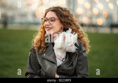 Jeune femme souriante tenant son chien blanc dans le parc Banque D'Images