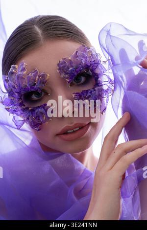Une belle jeune femme exprime sa créativité à travers un art de visage floral complexe et un tissu fluide. Banque D'Images