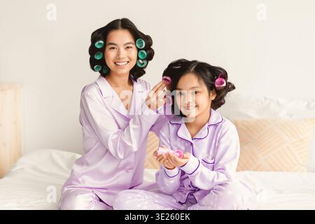Femmes et fille Styling cheveux avec bigoudis dans Pajamas à la maison le matin Banque D'Images