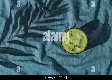 Scène de jour d'été avec latte matcha glacé et ombre de feuille de palmier tropical sur fond de lin de couleur bleu océan. Soleil et ombres. Banque D'Images