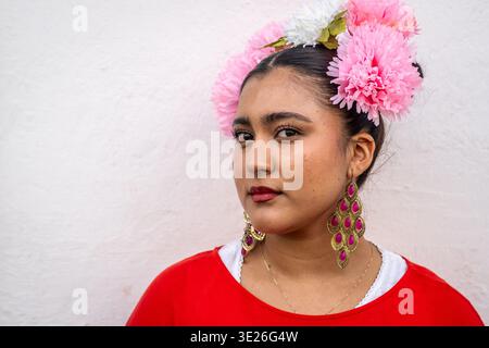 Festival de Flores - Antigua Guatemala - jeune femme guatémaltèque portant une couronne de fleurs roses, boucles d'oreilles ornées et chemisier rouge dans un portrait proche qui Banque D'Images