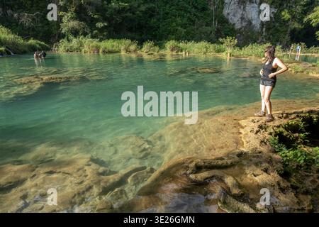Semuc Champey, Guatemala - Une femme en équipement de randonnée se tient sur un rebord de calcaire surplombant une piscine naturelle turquoise claire encadrée par des Fores tropicales luxuriantes Banque D'Images