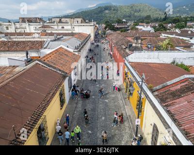 Vue aérienne d'une rue pavée animée à Antigua Guatemala bordée de bâtiments coloniaux colorés, touristes et habitants marchant sous terre cuite R Banque D'Images