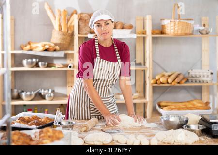 Femme travaille dans la boulangerie comme boulanger, pétrit la pâte, travaille avec la farine. Banque D'Images