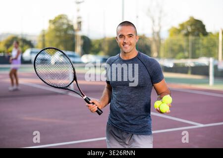 Joueur de tennis masculin plein d'entrain posant pour la caméra avec une raquette et une balle de tennis Banque D'Images