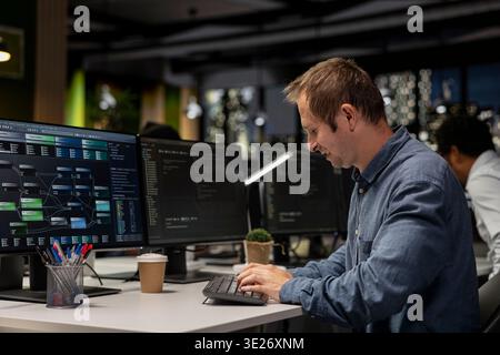 Ingénieur heureux au bureau examinant les métriques du système d'IA, surveillant les tableaux de bord de performance. Employé joyeux de la société de technologie accordant des réseaux neuronaux à l'aide d'un programme sur l'ordinateur Banque D'Images