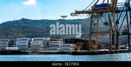 Conteneurs maritimes commerciaux et grues industrielles au port de Carthagène, Espagne, avec un paysage vallonné et un ciel bleu vif en arrière-plan. Banque D'Images