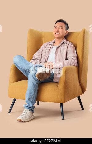 Jeune homme asiatique assis dans un fauteuil sur fond beige Banque D'Images