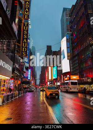 Regardant vers le bas de la 42ème rue de New York par une soirée pluvieuse, sombre et orageuse. Les panneaux d'affichage à LED multiples projettent des reflets sur la route humide Banque D'Images