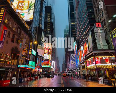 Regardant vers le bas de la 42ème rue de New York par une soirée pluvieuse, sombre et orageuse. Les panneaux d'affichage à LED multiples projettent des reflets sur la route humide Banque D'Images