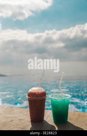 Deux boissons fraîches colorées sur le bord de la piscine à débordement avec l'horizon de l'océan et le ciel doux créant la scène de rafraîchissement de l'été Banque D'Images